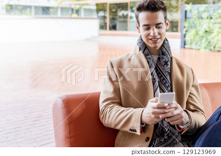 Smiling young man using phone on modern leather sofa 129123969
