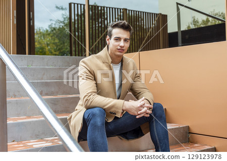 Confident young man sitting on modern outdoor steps Confident young man sitting on modern outdoor steps 129123978