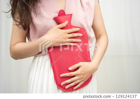 Woman using hot water bottle to relieve menstrual abdominal pain. 129124137