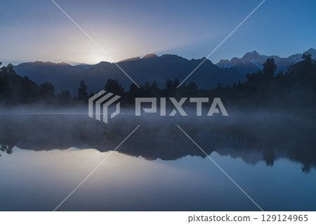 Mount Cook and the rising sun seen from misty Lake Matheson in the early morning in New Zealand Mount Cook and the rising sun seen from misty Lake Matheson in the early morning in New Zealand 129124965