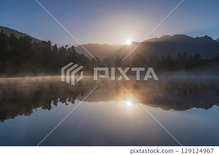 Mount Cook and the rising sun seen from misty Lake Matheson in the early morning in New Zealand Mount Cook and the rising sun seen from misty Lake Matheson in the early morning in New Zealand 129124967
