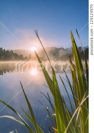 Mount Cook and the rising sun seen from misty Lake Matheson in the early morning in New Zealand Mount Cook and the rising sun seen from misty Lake Matheson in the early morning in New Zealand 129124970
