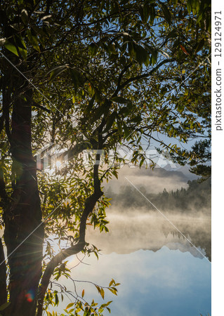 Mount Cook and the rising sun seen from misty Lake Matheson in the early morning in New Zealand Mount Cook and the rising sun seen from misty Lake Matheson in the early morning in New Zealand 129124971