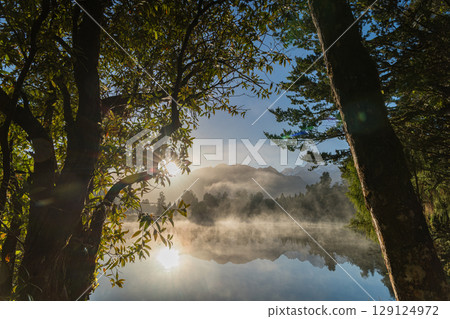 Mount Cook and the rising sun seen from misty Lake Matheson in the early morning in New Zealand Mount Cook and the rising sun seen from misty Lake Matheson in the early morning in New Zealand 129124972