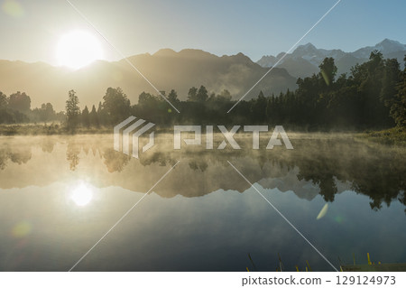 Mount Cook and the rising sun seen from misty Lake Matheson in the early morning in New Zealand Mount Cook and the rising sun seen from misty Lake Matheson in the early morning in New Zealand 129124973