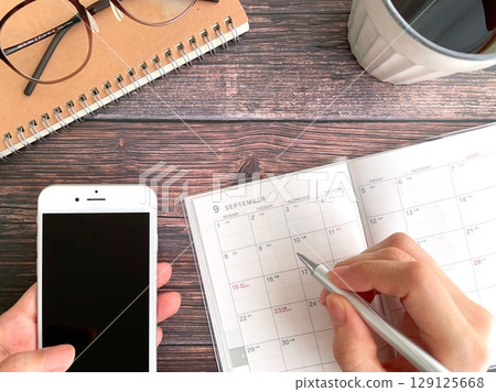 A woman holding a smartphone and filling out her schedule for September 129125668