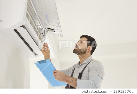 Technician with screwdriver checking air conditioner system and providing maintenance at client home Technician with screwdriver checking air conditioner system and providing maintenance at client home 129125703