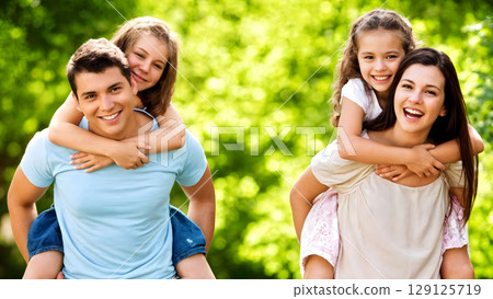 Happy family enjoying outdoor time with parents giving piggyback rides to their smiling children in bright sunny park 129125719