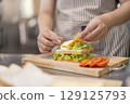 Hand placing slice of cheese on homemade sandwich. 129125793