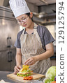 A young Asian woman placing slice of cheese on homemade sandwich. 129125794