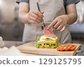 Hand using a spoon to add ham on a sandwich. 129125795