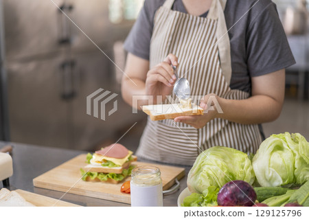 Woman spreading mayonnaise on bread for a sandwich. 129125796