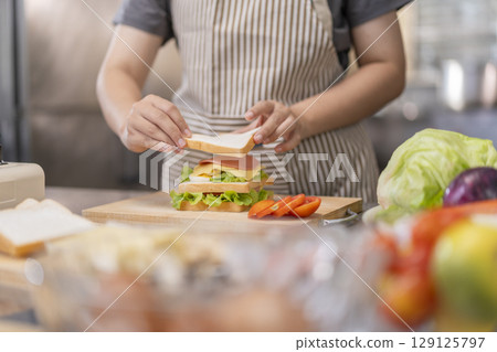 Hands placing final slice of bread on a sandwich. 129125797