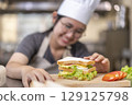 Asian Female Chef Assembling Fresh Sandwich in Kitchen 129125798