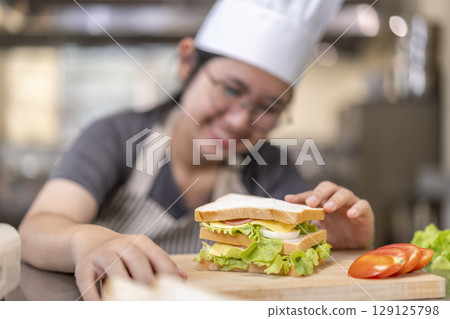 Asian Female Chef Assembling Fresh Sandwich in Kitchen Asian Female Chef Assembling Fresh Sandwich in Kitchen 129125798