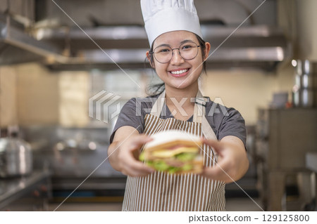 Smiling Asian Female Chef Holding Sandwich in Kitchen 129125800