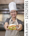 Smiling Asian Female Chef Holding Sandwich in Kitchen 129125801
