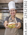 Smiling Asian Female Chef Holding Sandwich in Kitchen 129125802