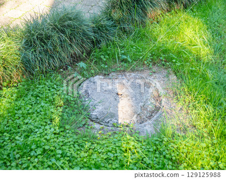 Stone sewer manhole next to the grass. Entrance to underground communications 129125988