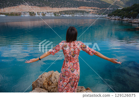 Woman in red Outfit Looking Out Over Cliff Into Water Woman in red Outfit Looking Out Over Cliff Into Water 129126075