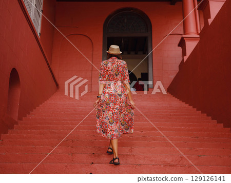 woman in dress and hat exploring vibrant streets of Malacca, Malaysia. 129126141