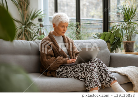 A woman is sitting on a couch and using a laptop 129126858