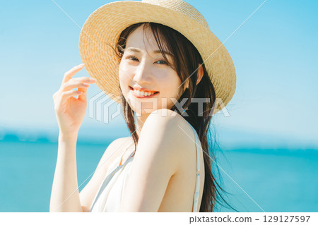 A woman wearing a straw hat with the sea and blue sky in the background 129127597