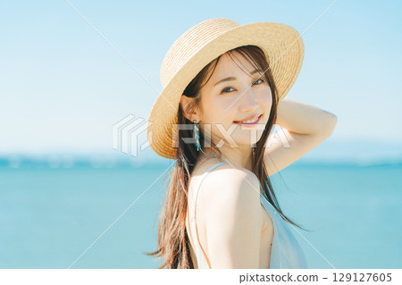 A woman wearing a straw hat with the sea and blue sky in the background 129127605