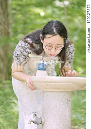 Young woman drinking water at a drinking fountain in the park 129127873
