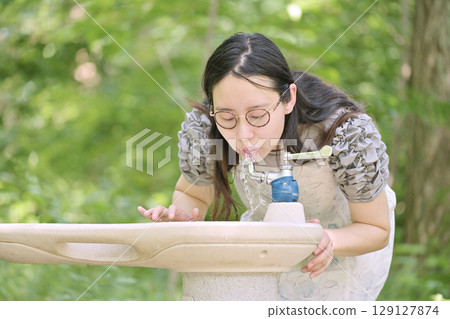 年輕女子在公園飲水機邊喝水 129127874