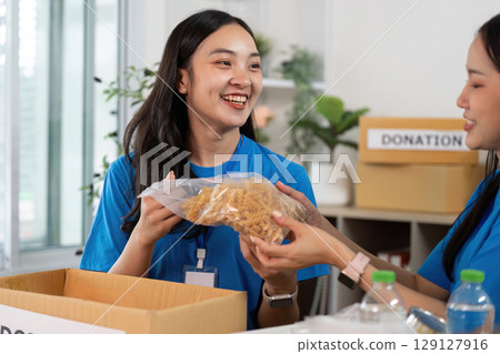 Volunteer engagement. Woman presenting food donation to her teammate with joy. 129127916