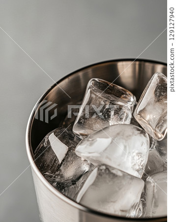Close-up of crystal-clear ice cubes in a metal cup on neutral gray background 129127940