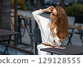 Outdoor portrait of a young stylish Caucasian woman sitting in sidewalk cafe. Vacation summer mood. 129128555