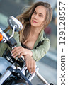 Young beautiful Caucasian biker-woman posing on her bike after driving and looking at camera. Femininity and the spirit of travel rolled into one. 129128557