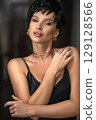 Close-up vertical portrait of a sensual Caucasian young woman. Young sexy short haired brunette woman looking at camera. Skin care concept. Photo with copy space over dark background. 129128566