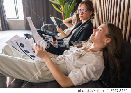 Female team enjoying a quiet office moment, working casually and bonding on the sofa 129128581