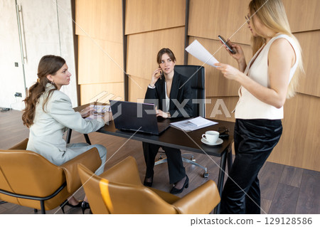 Consulting team of businesswomen working with documents in modern office interior 129128586