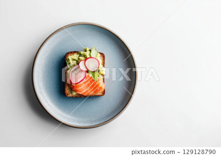 Gourmet open sandwich with avocado, salmon, radish, and greens served on a blue plate. Ideal for restaurant menus, healthy food blogs, catering ads, or modern culinary presentations. Copy space 129128790