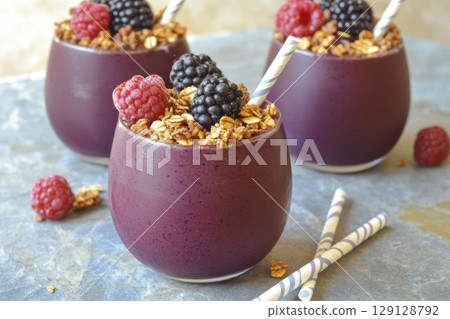Vibrant berry smoothie in a glass topped with granola, raspberries, and blackberries. Served with a pink striped straw. Perfect for healthy lifestyle blogs, ads, menus, or social media content. 129128792
