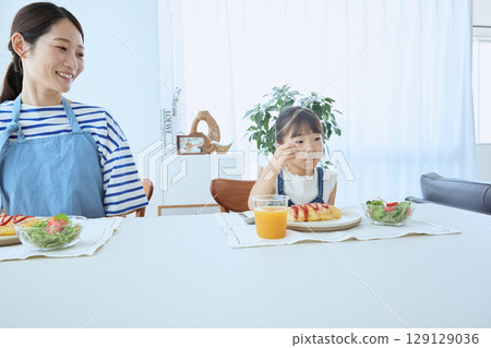 Mother and daughter watching over their child's meal, enjoying a warm breakfast 129129036