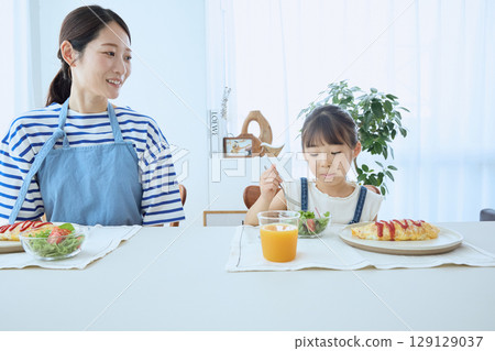 Mother and daughter watching over their child's meal, enjoying a warm breakfast Mother and daughter watching over their child's meal, enjoying a warm breakfast 129129037