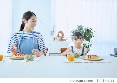 Mother and daughter watching over their child's meal, enjoying a warm breakfast 129129045
