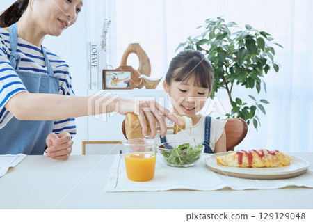 Mother and daughter watching over their child's meal, enjoying a warm breakfast 129129048