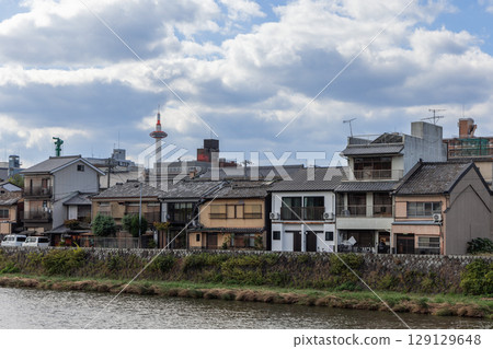 Traditional wooden houses stand along the Kamo River in Kyoto with Kyoto Tower rising behind 129129648