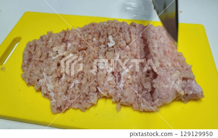 Fresh Minced Meat Chopped on Yellow Cutting Board with Sharp Knife in Kitchen Setting 129129950