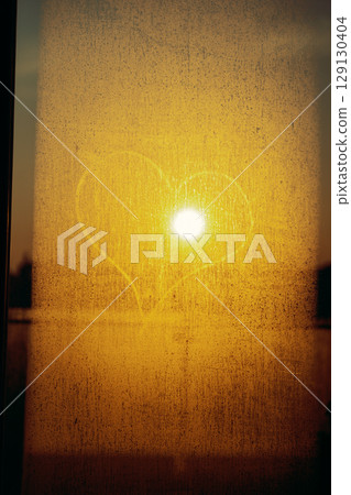 Heart shape drawn on foggy window at sunset with golden sun shining through glass Heart shape drawn on foggy window at sunset with golden sun shining through glass 129130404