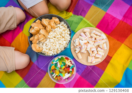 Childrens picnic with popcorn, sweets and jelly pastries on colorful blanket 129130408