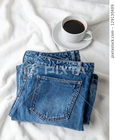 Stack of Blue Denim Jeans with White Coffee Cup on a White Textile Background 129130489
