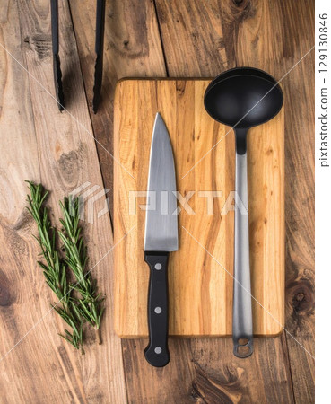 Wooden Cutting Board with Knife Ladle and Rosemary on Rustic Table Overhead 129130846