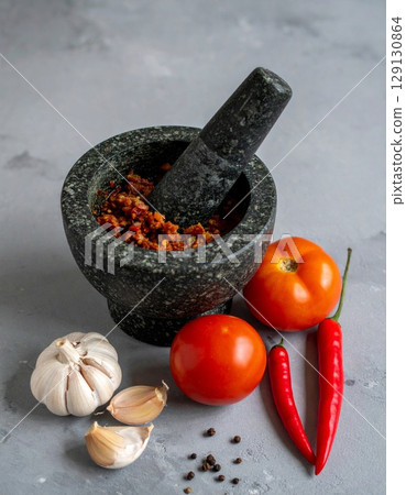 Granite Mortar with Pestle with Spicy Mixture and Raw Ingredients on Gray Surface 129130864